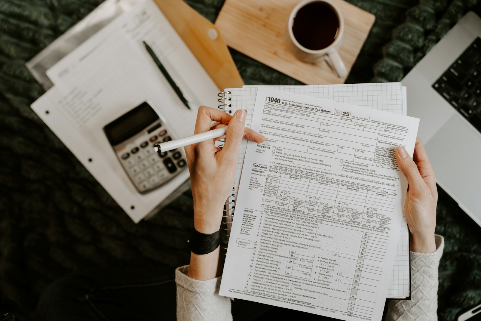 Person reviewing financial documents with calculator, pen, and laptop nearby.