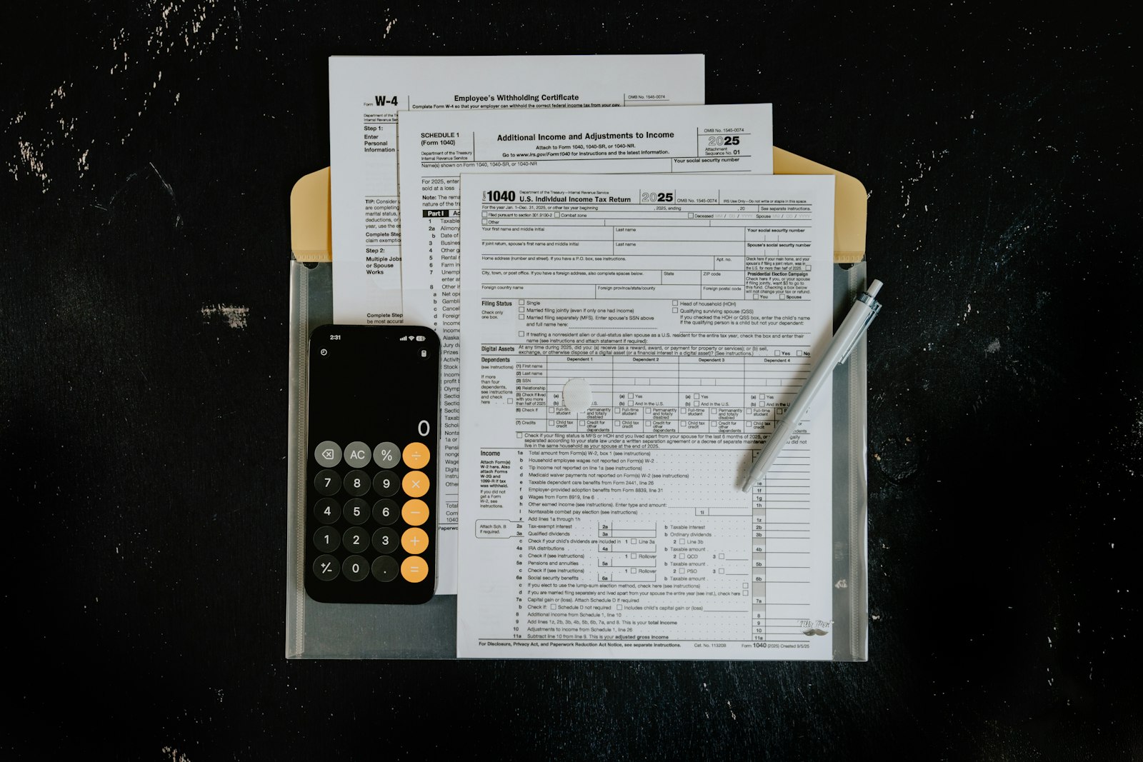 Tax forms, calculator, and pen arranged on a dark desk.