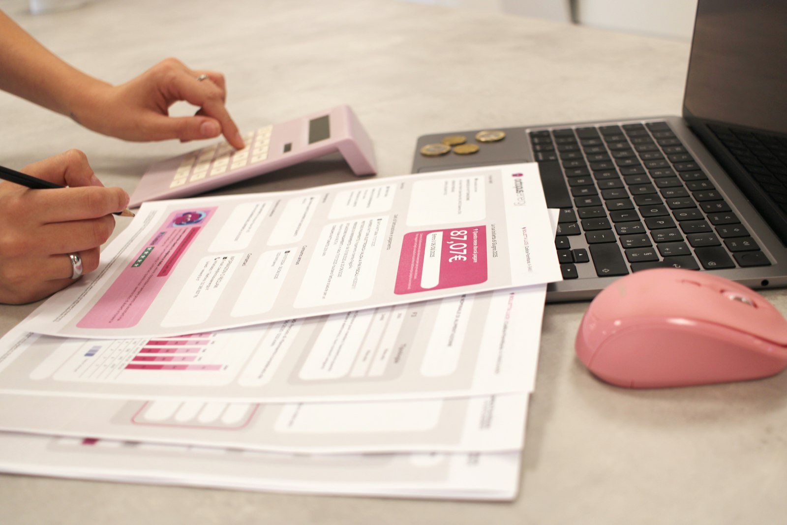 Woman calculating bills with paperwork, laptop, and calculator on a desk.